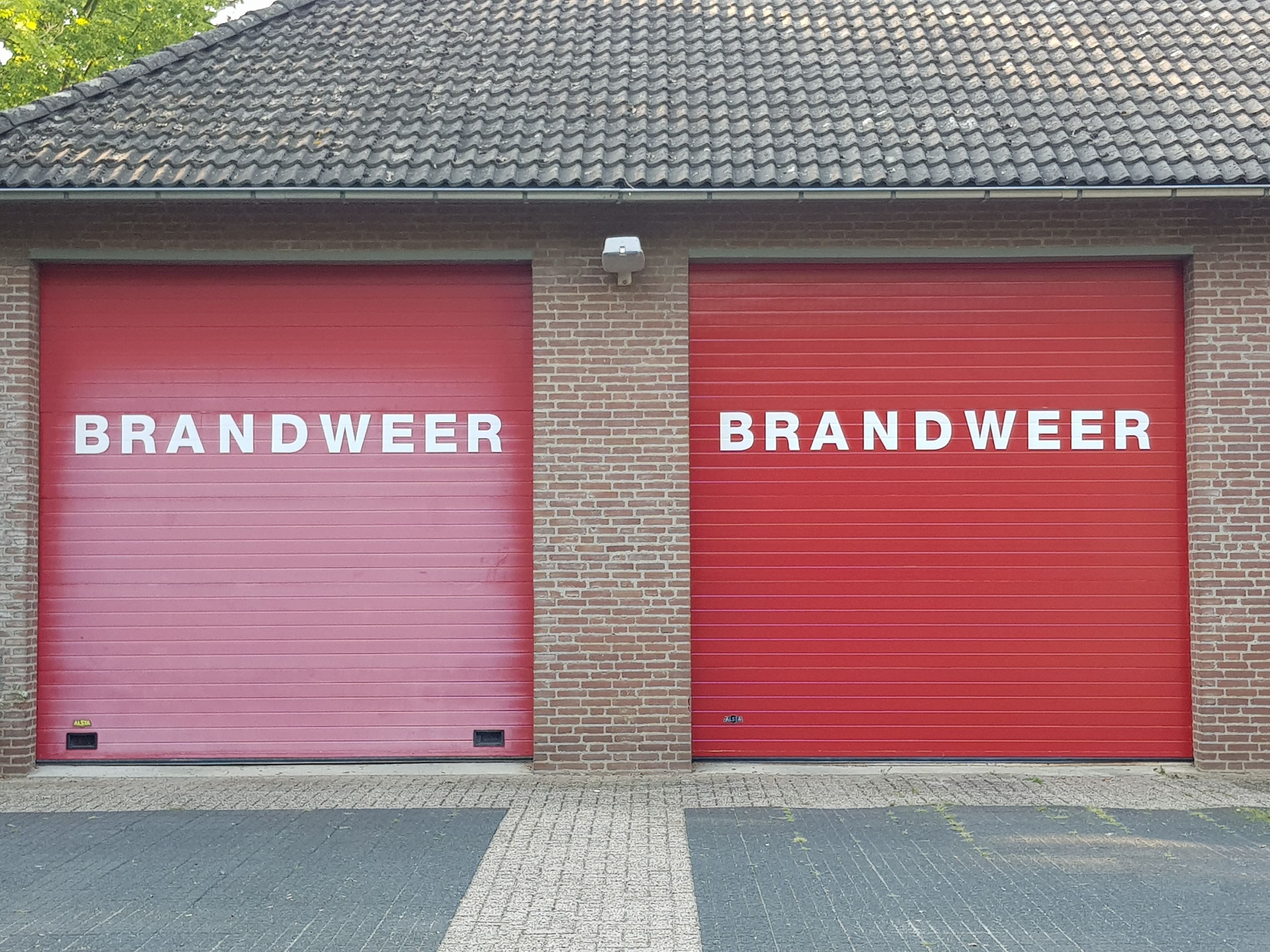 Twee rode garagedeuren met BRANDWEER-belettering van een brandweerkazerne