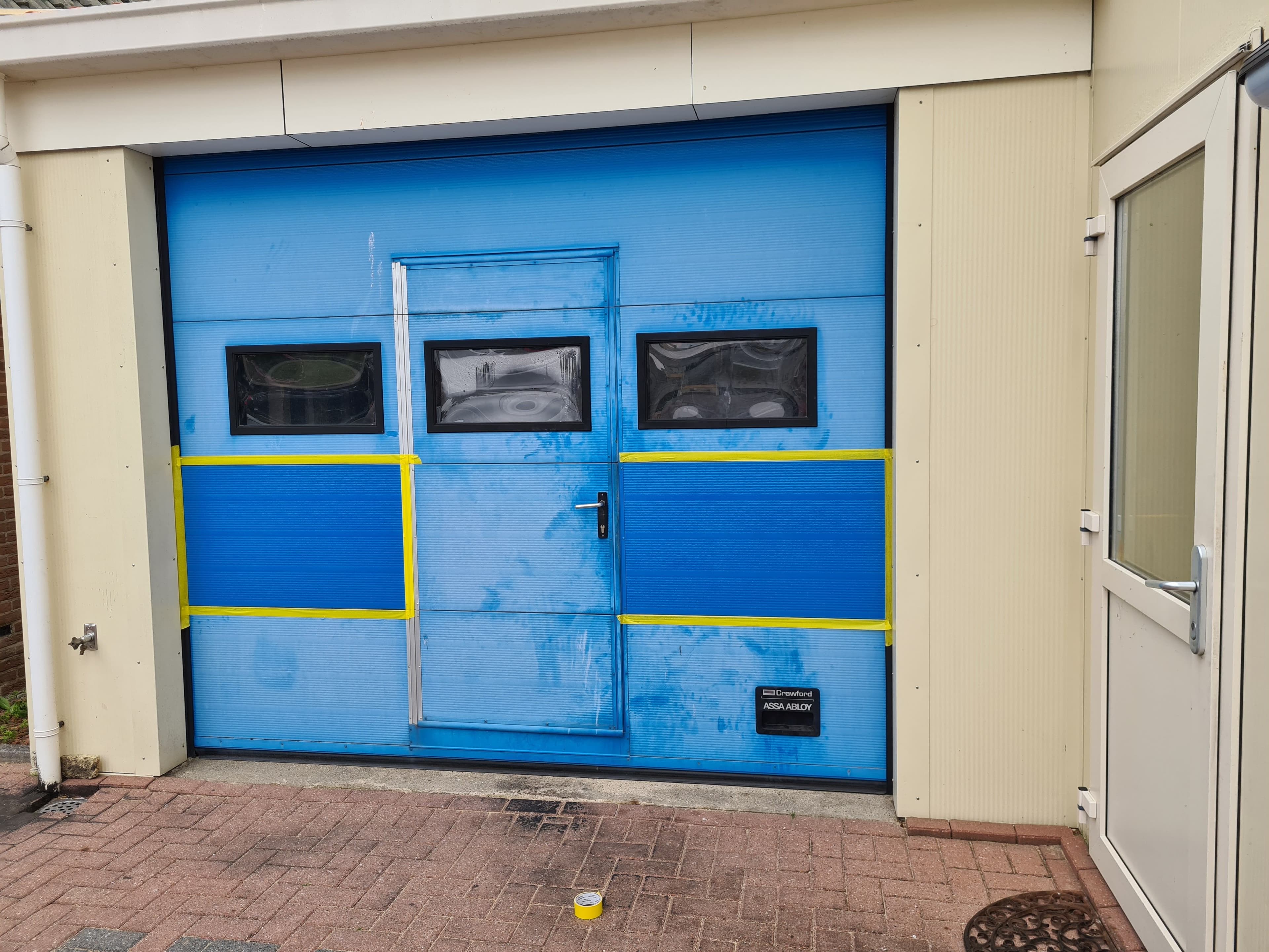 Blauwe garagedeur op Texel met een afgeplakt coatingproefvlak